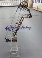 Tan compound bow on a clear stand inside an archery range
