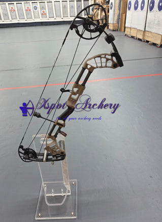 Tan compound bow on a clear stand inside an archery range